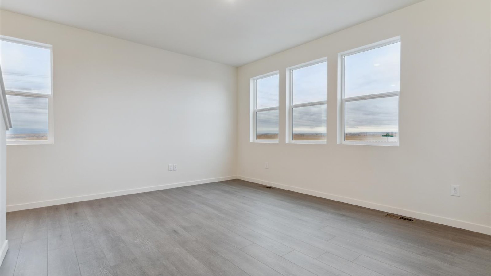 Open Edmon floor plan living room with hardwood flooring and three windows for ample lighting