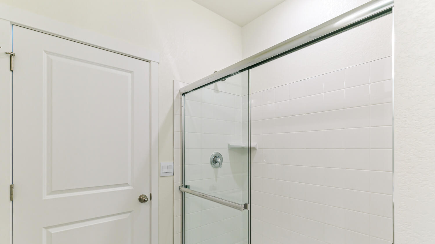 Step-in shower in private bathroom with glass sliding door and white tile