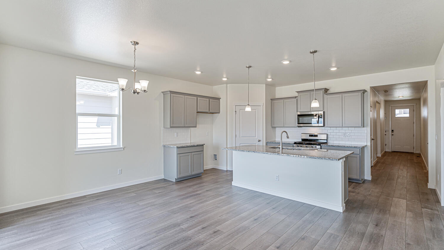 View of foyer and hallway leading to open kitchen with large island, ample lighting, premium cabinetry and corner pantry