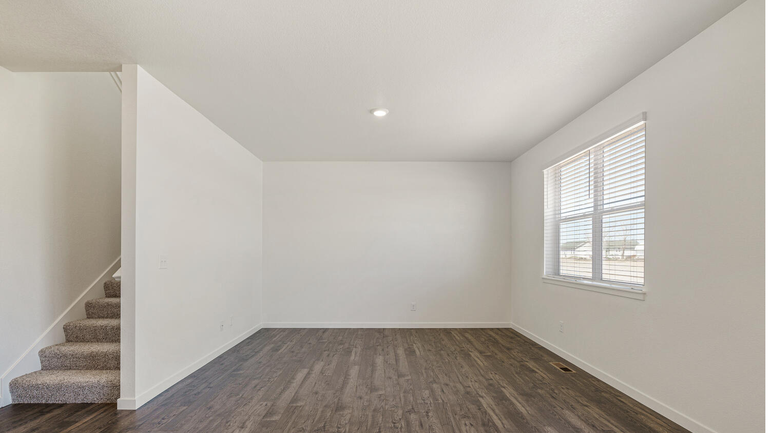 View of great room from dining area with ample lighting and stairwell to upper floor