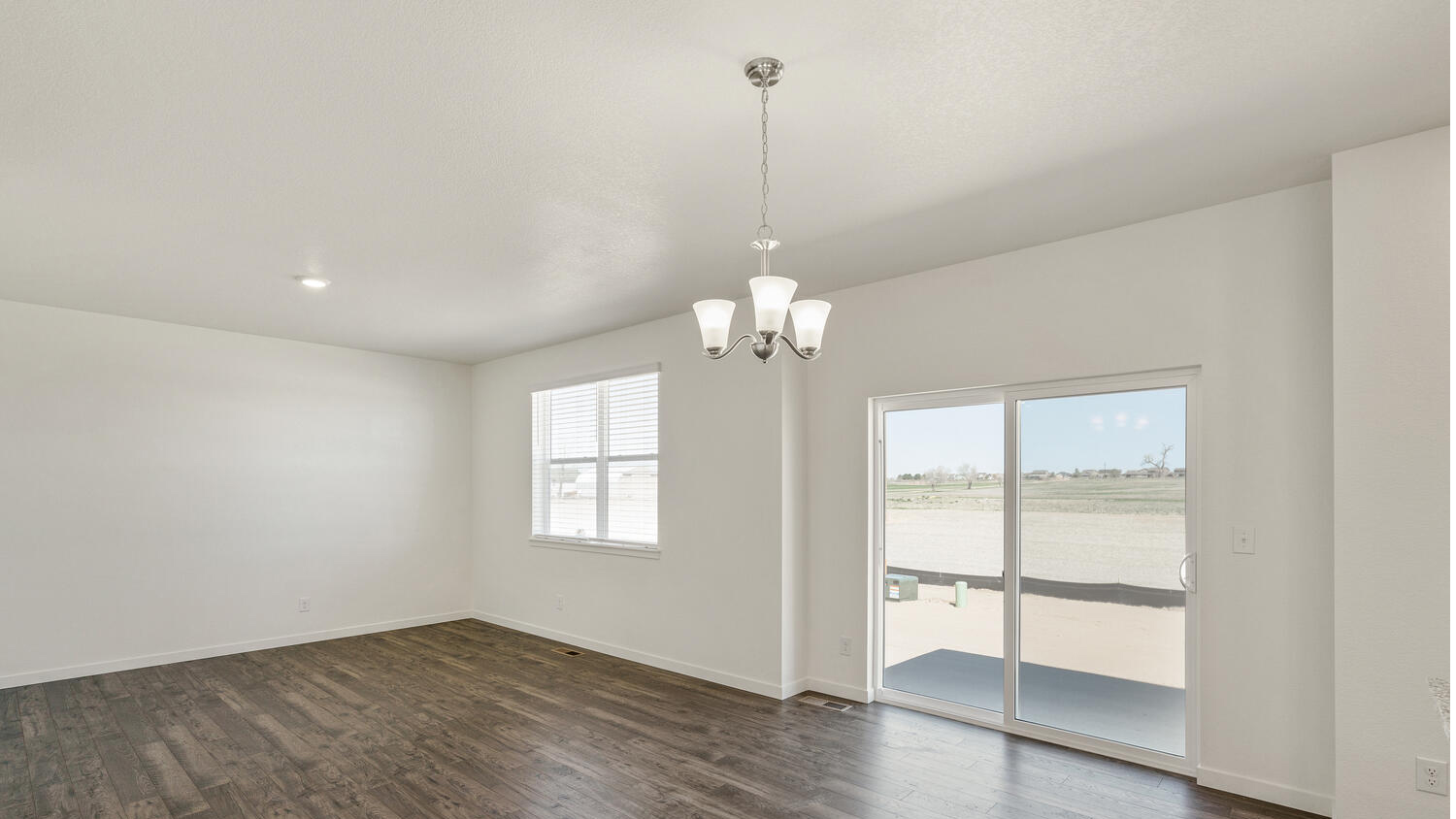 Zoomed out corner view of great room extended to dining area with chandelier light fixture and sliding door to patio outside