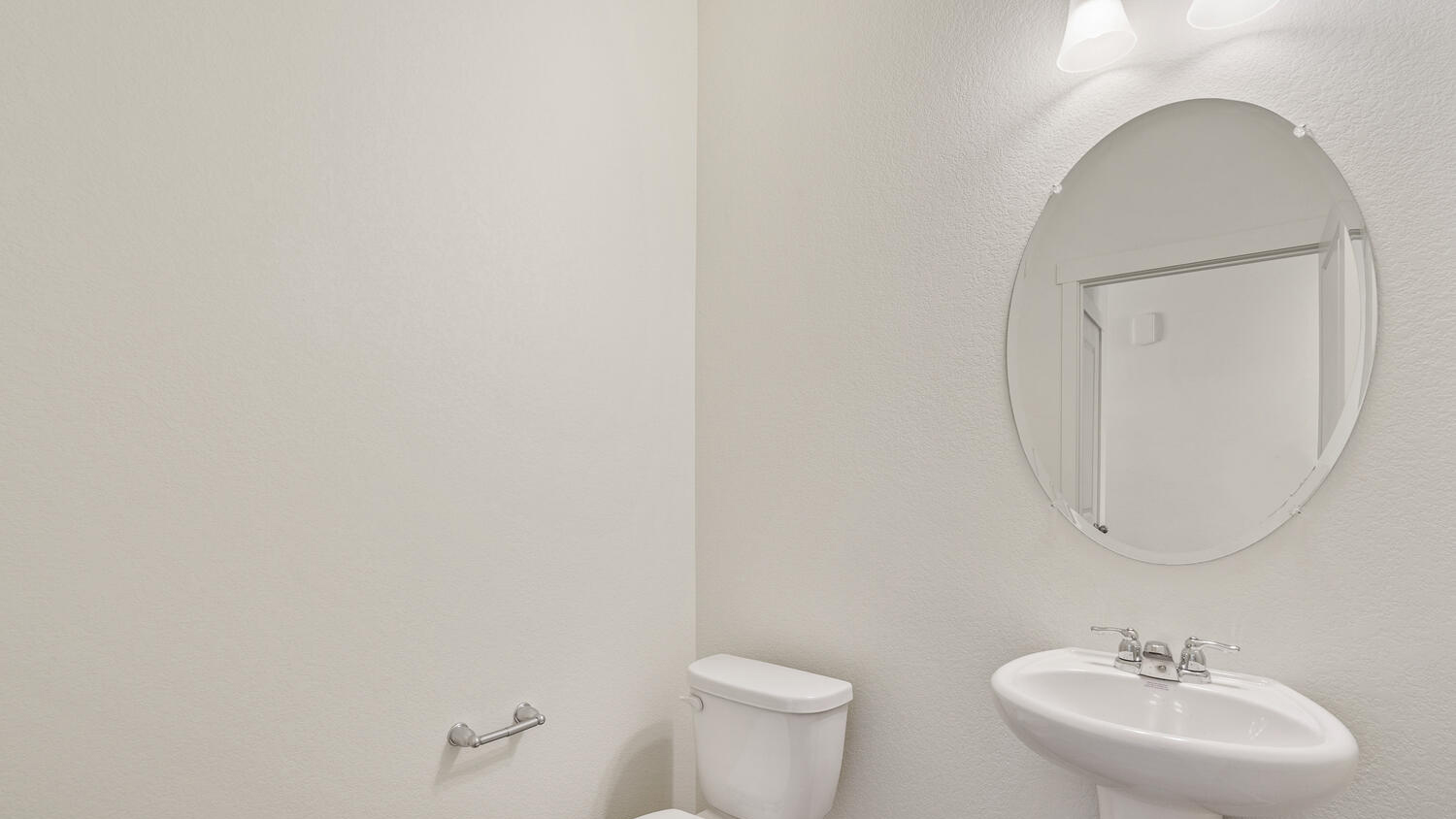 Powder room near stairwell and coat closet with vanity lighting, pedestal sink, oval mirror, and chrome light fixtures