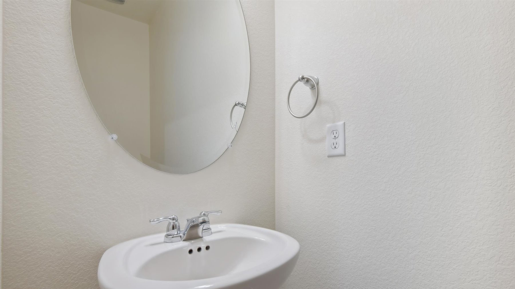Pedestal sink, oval mirror, and chrome faucet in main floor powder room adjacent to coat closet