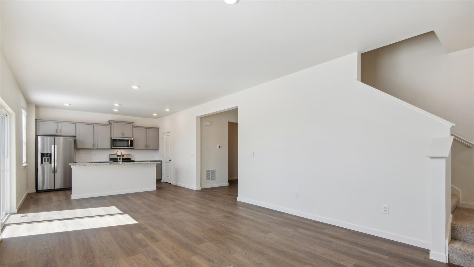 Another view of kitchen connected with dining area and great room with hallway entry and upper floor stairwell