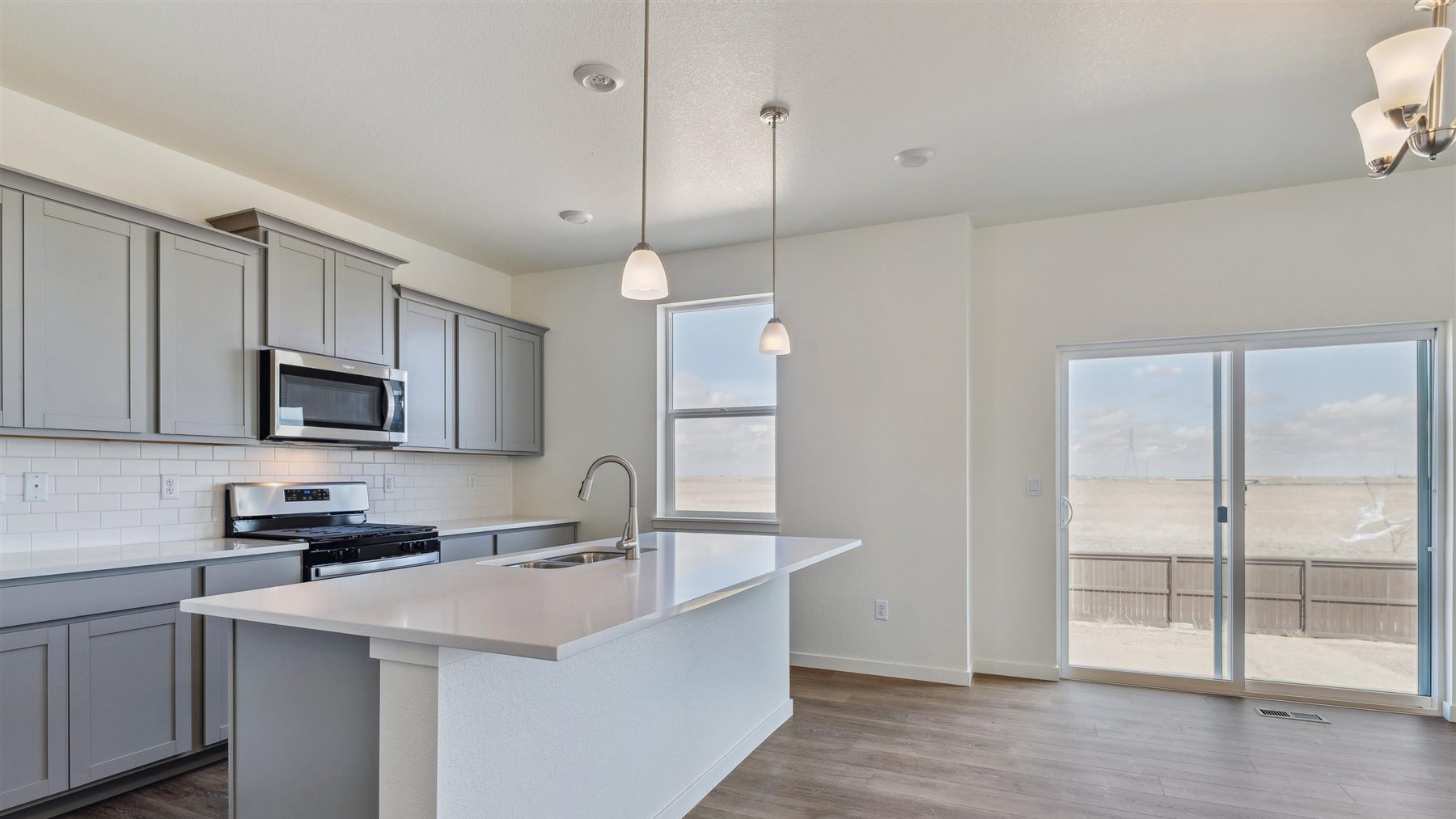 Corner view of sliding porch door in dining nook and kitchen with pendant lighting above center island