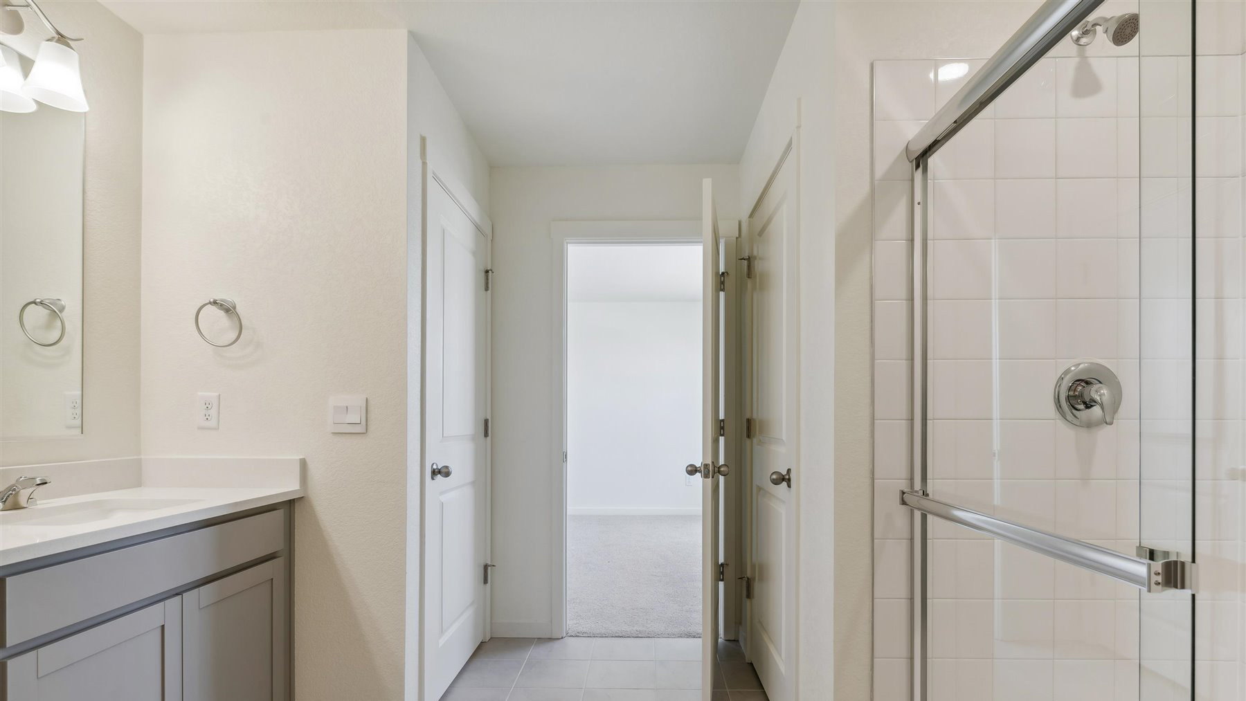 Alternate view of primary bedroom private bath showing water closet near step-in shower, dual vanity sinks, and linen closet