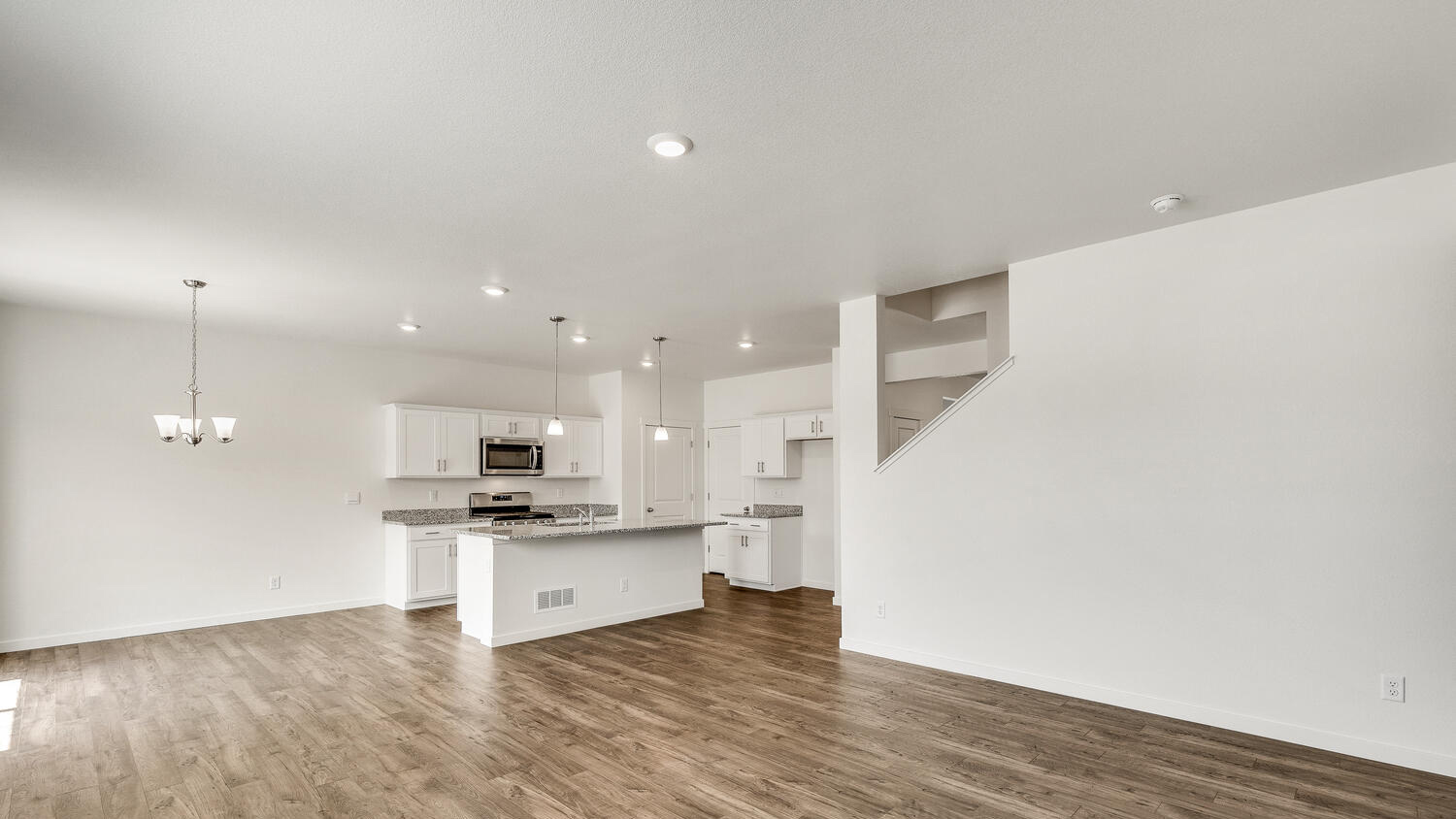 Main floor open concept living area, including kitchen, dining, and great room, and half wall showing upper floor stairwell