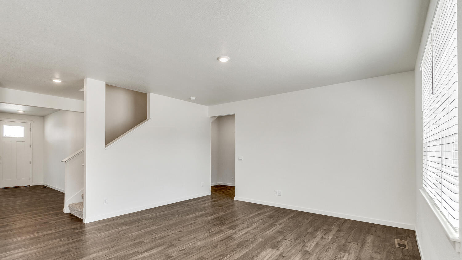 Angle view of great room showing upper floor stairwell, foyer and front door entry, and opening to secondary bedroom and bath