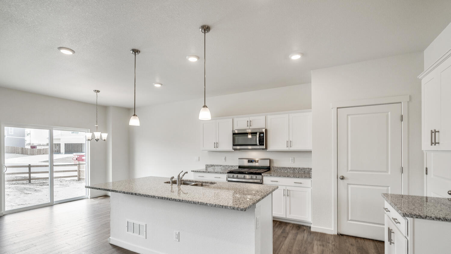 Alternate kitchen image showing connected dining area and sliding patio door, along with ample suspended and LED lighting