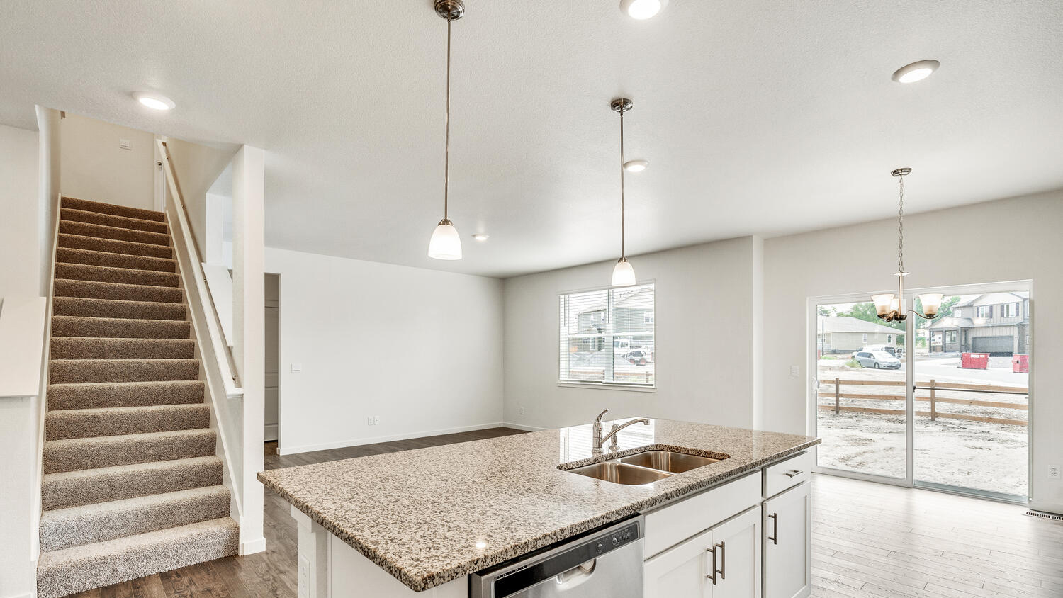 Kitchen island with granite countertop and built in sink, open to dining area and great room with stairwell nearby