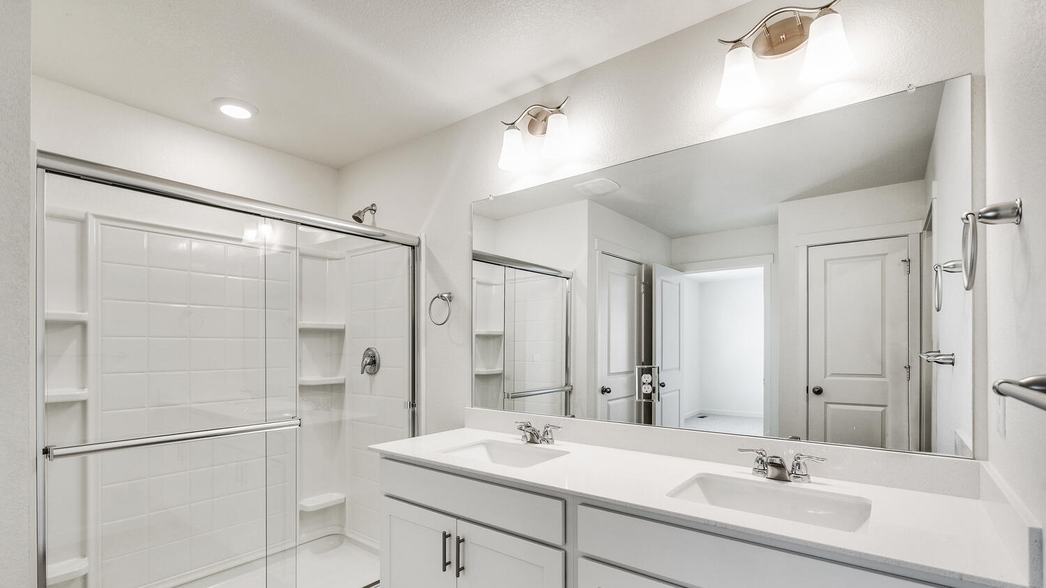 Private bathroom in primary bedroom suite with dual vanity sinks, chrome finishes, and walk-in shower