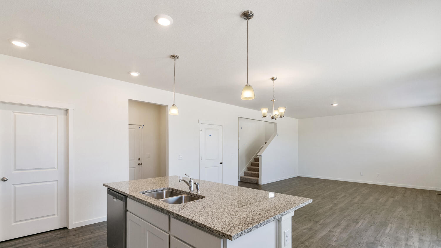Corner view of kitchen island with large counterspace, built-in sink, and pendant lighting open to great room and dining area