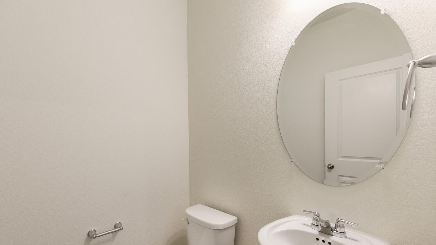 Main floor powder room with oval mirror, pedestal sink, vanity lighting, and chrome fixtures