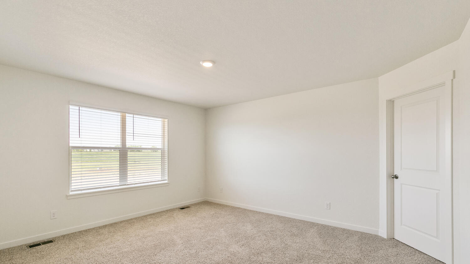 Large window and plush carpeting in primary bedroom suite with door to private bathroom