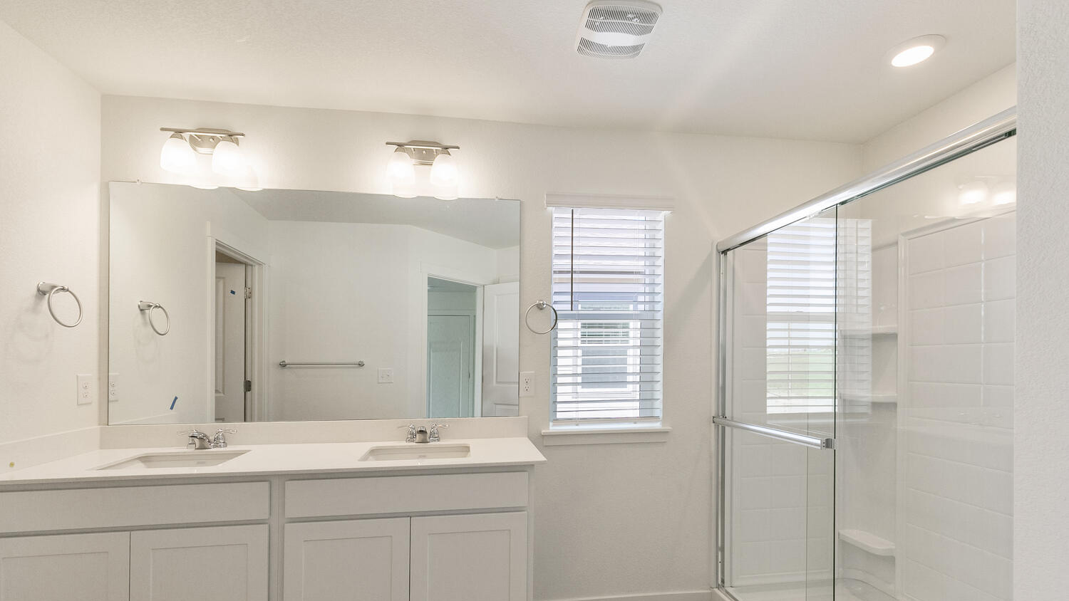 Private bath in primary bedroom suite with dual vanity sinks, large mirror, window, and step-in shower