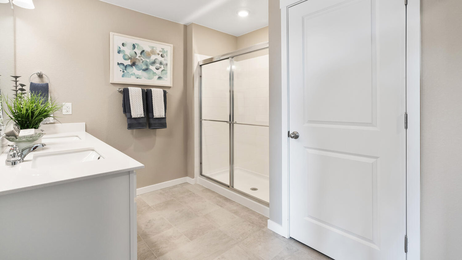 Corner view of primary bedroom private bath with water closet, double sinks with vanity light fixtures, and step-in shower
