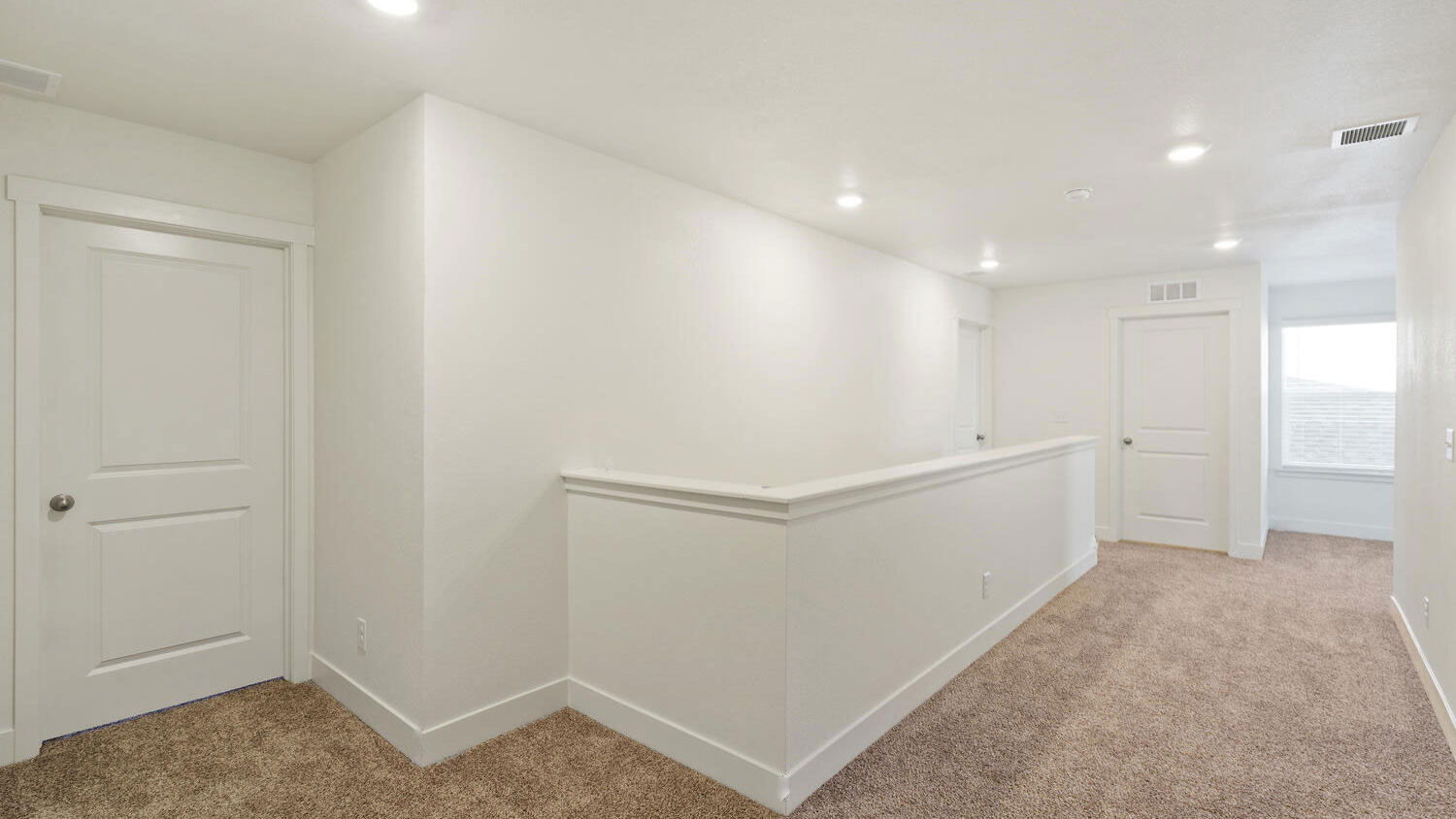 Upper floor hallway showing door to secondary bedroom, stairwell, and laundry room at top of stairs