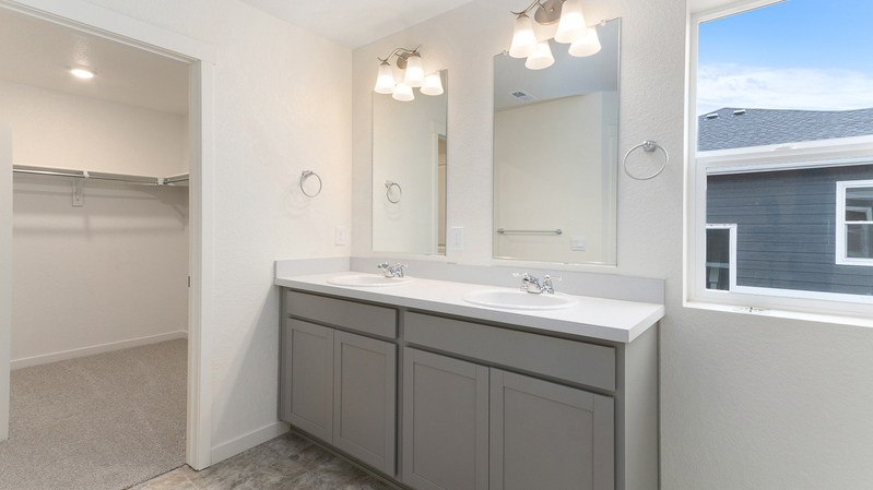 Dual vanity sinks and window in private bathroom with connected walk-in closet