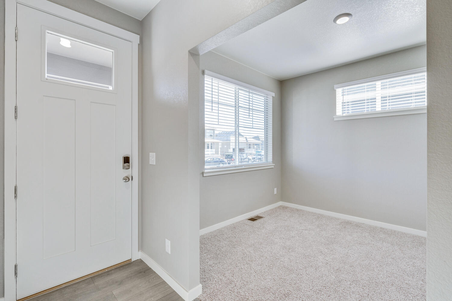 Foyer leading into carpeted study facing front of house. Two windows and overhead lighting brighten the room