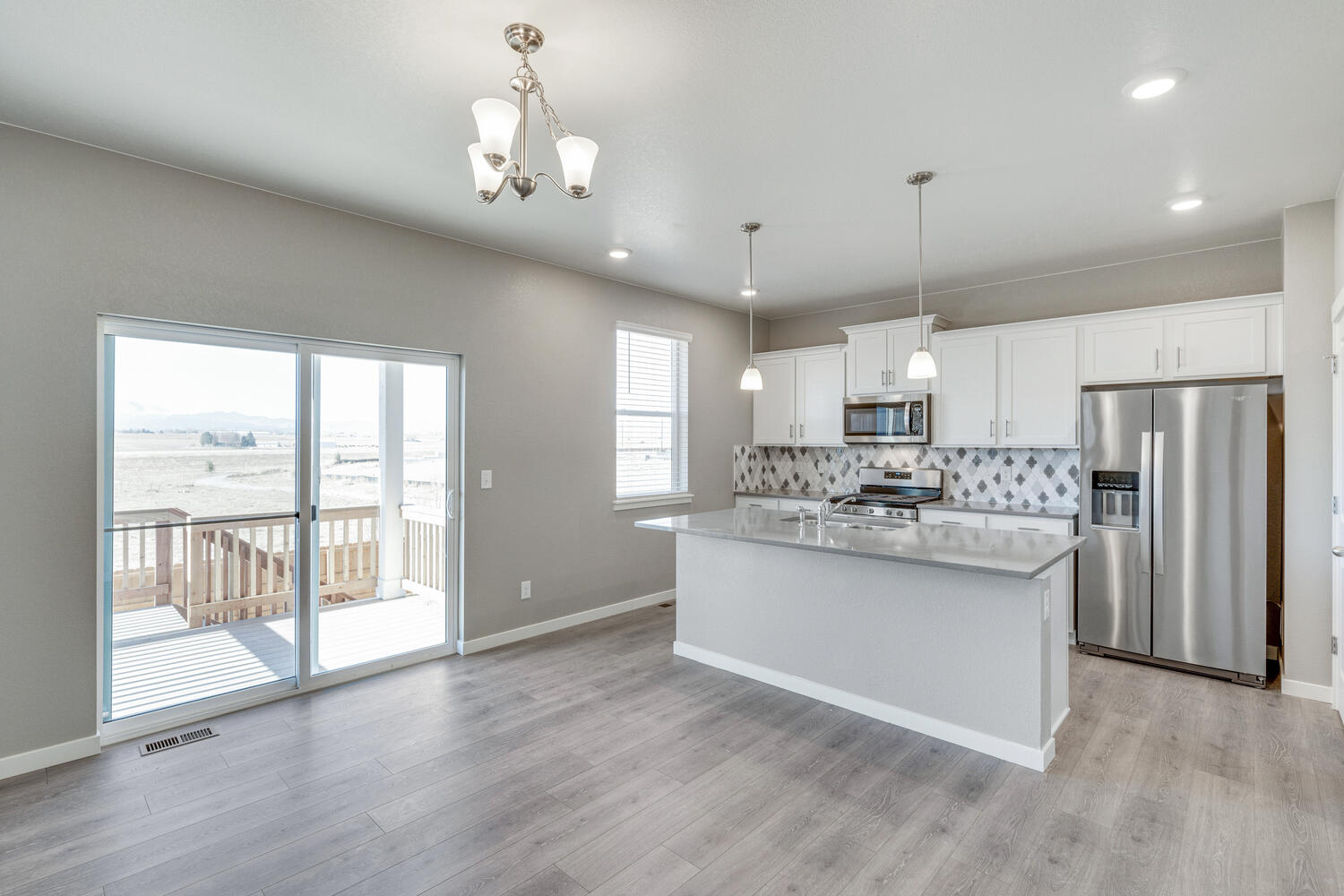 Dining area and kitchen with slighting glass door in background. A chandelier hangs over the nook and two hanging light fixtures hang over the island.