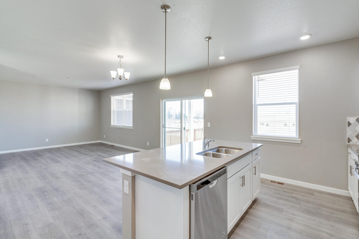 View of ground floor behind the island with great room, dining nook in background warmed by plenty of light fixtures