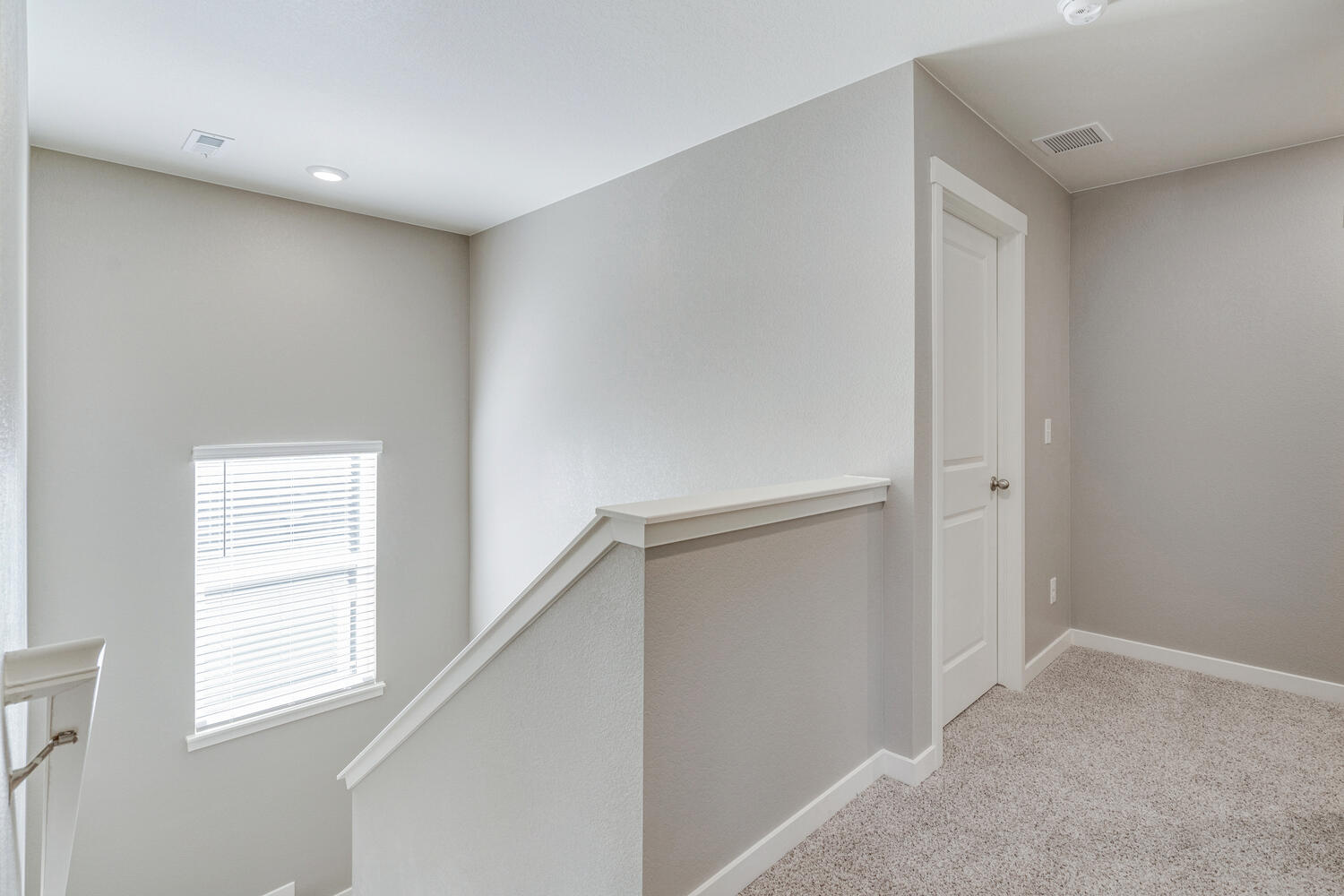 Second floor stairwell landing carpeted floor, and natural and overhead lighting.