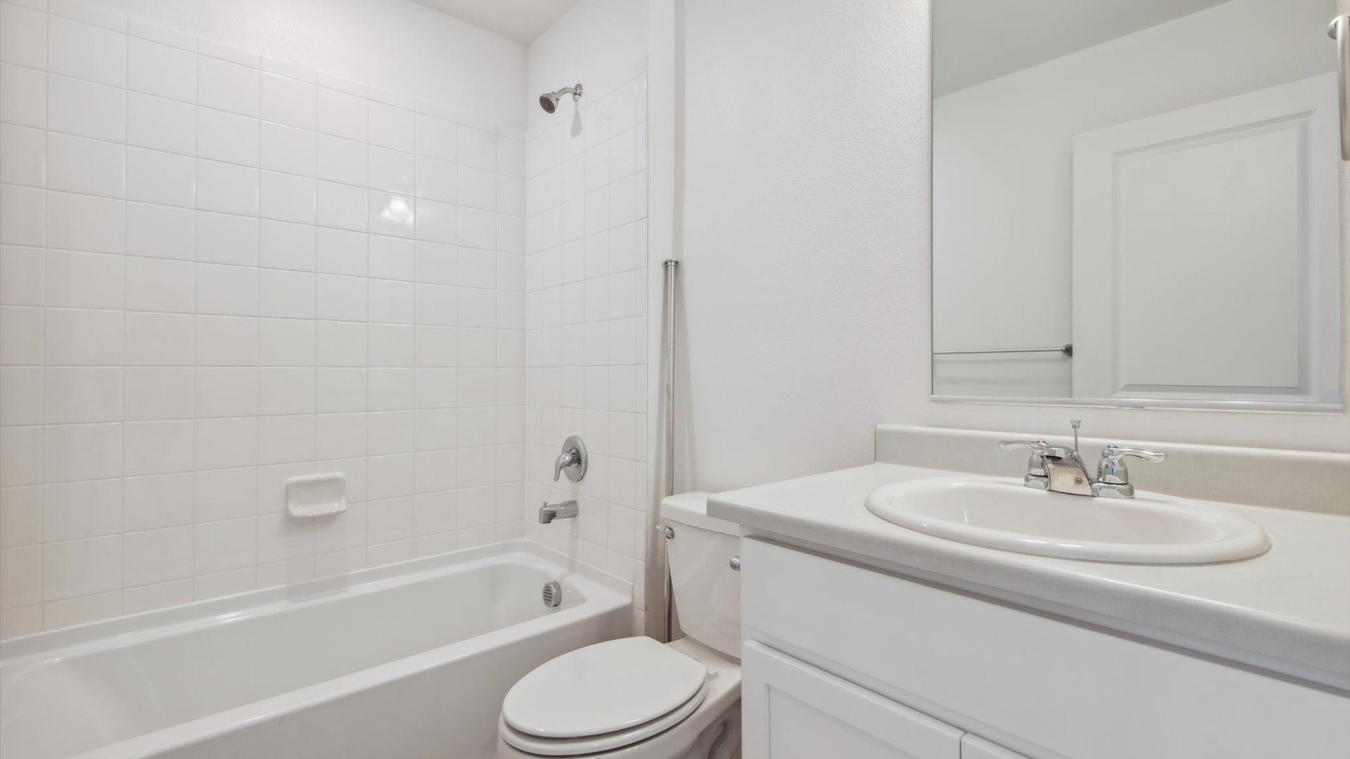 Shared hallway bathroom displays a white vanity cabinet and counter with oval sink, chrome faucet and combination tub-shower