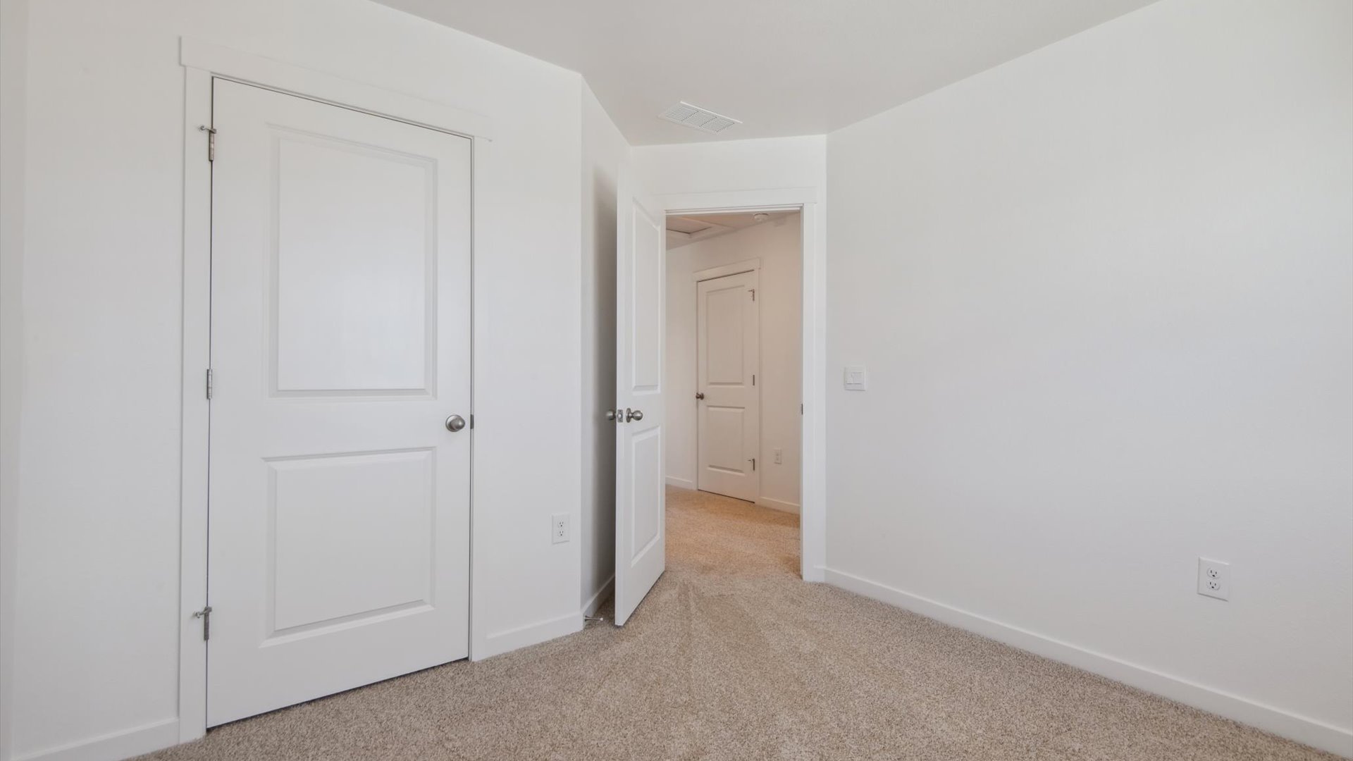 Secondary bedroom in the Douglas floor plan with spacious storage closet, deako light switches and linen closet in hallway