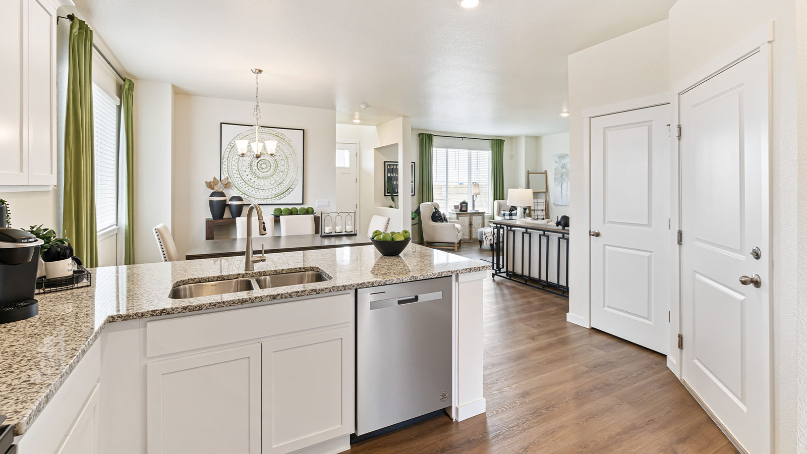 Alt angle view of kitchen peninsula and undermount sink in Alamosa home design with dining room and great room visible behind