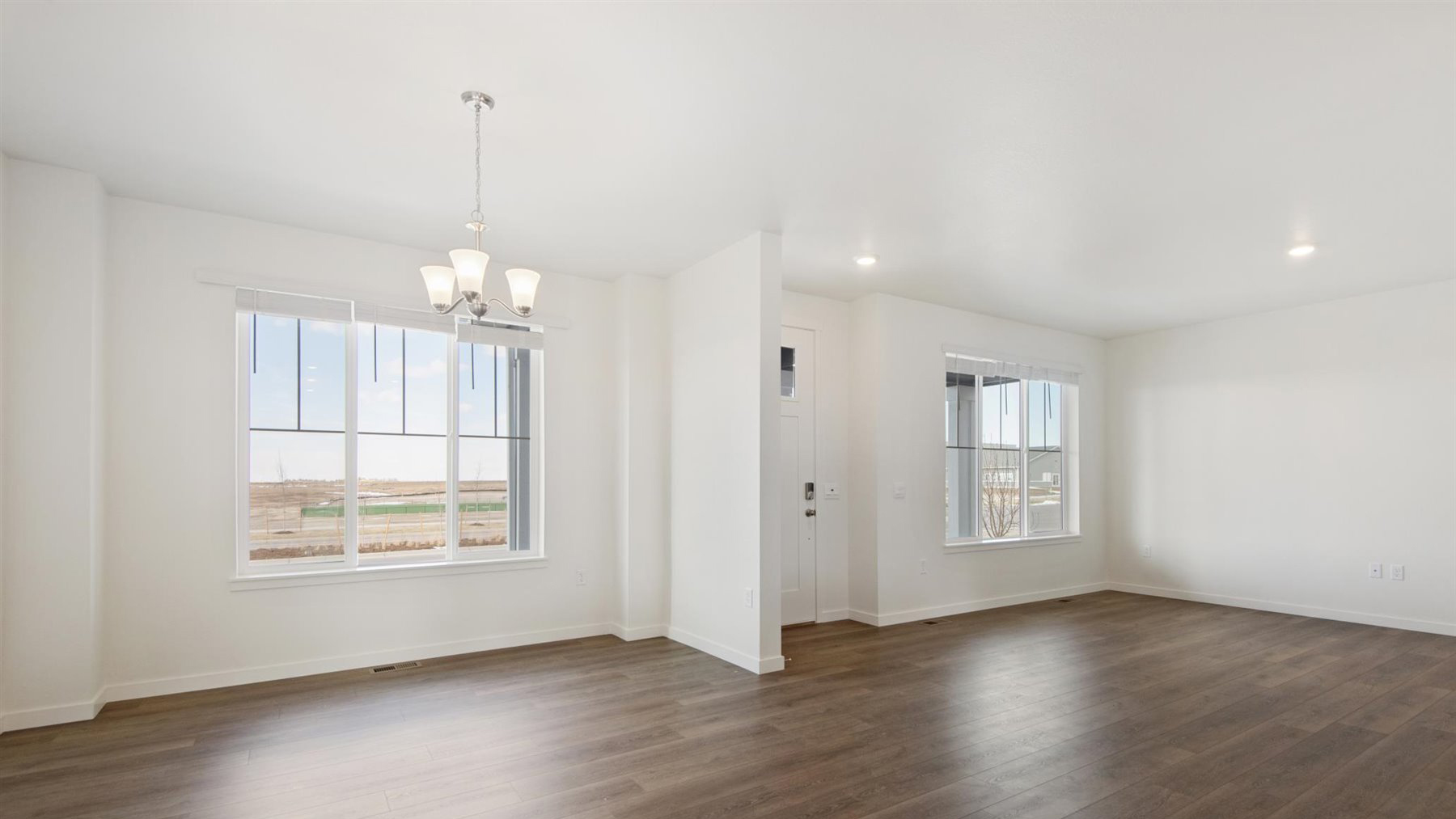 Elegant dining room in Elbert floor plan with multiple tall gridded windows, brushed nickle chandelier and great room behind