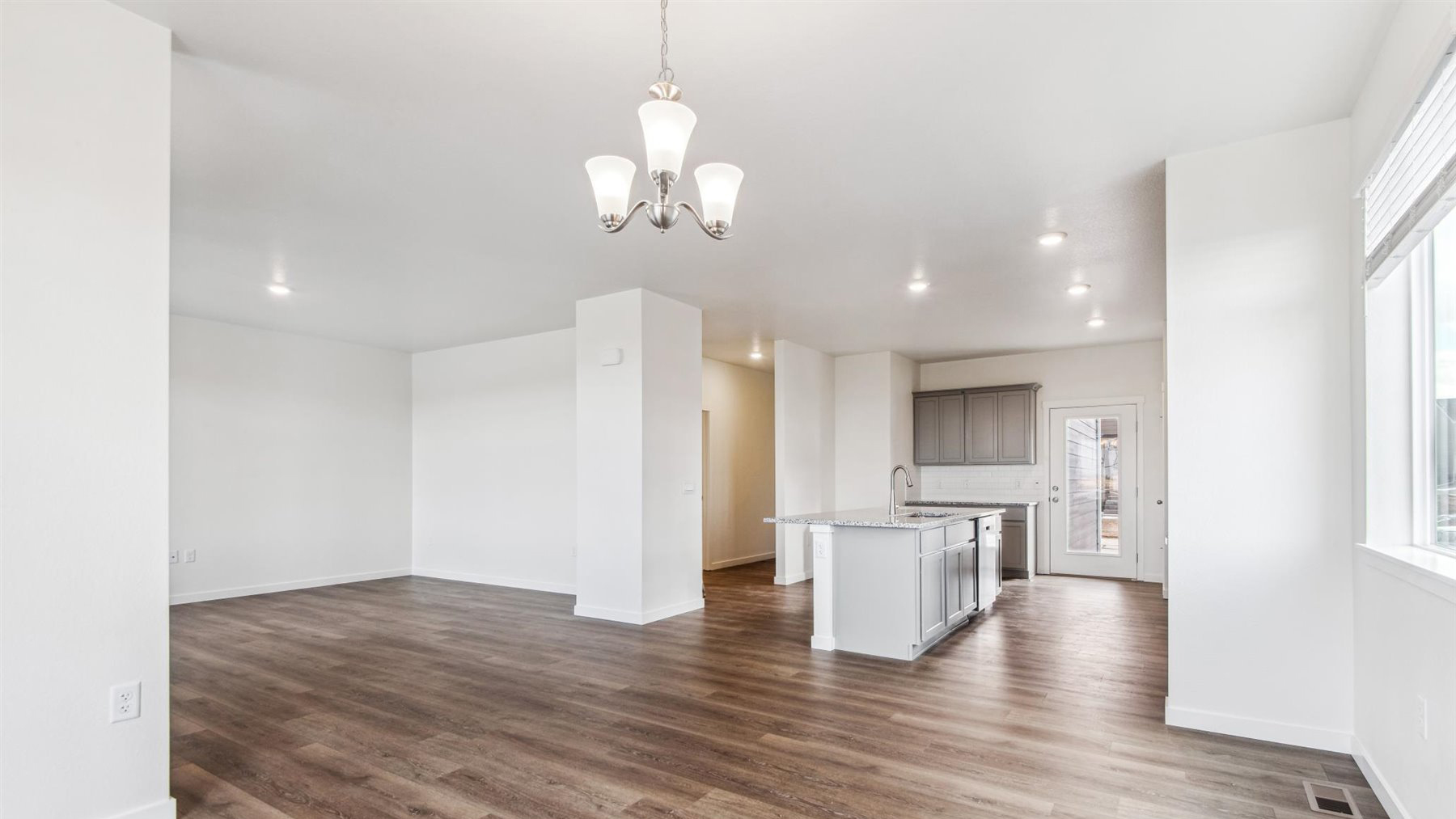 From dining room of Elbert floor plan, looking toward kitchen and great room, showcasing expansive warm tone hardwood floors