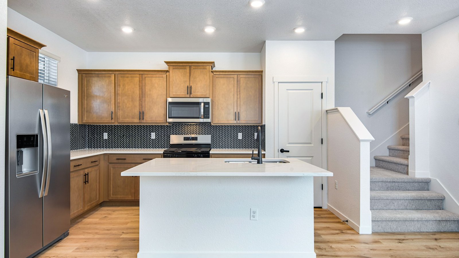 Open-concept kitchen with warm brown cabinets, black finishes, and contemporary styling in Horizon Uptown Muirfield home.