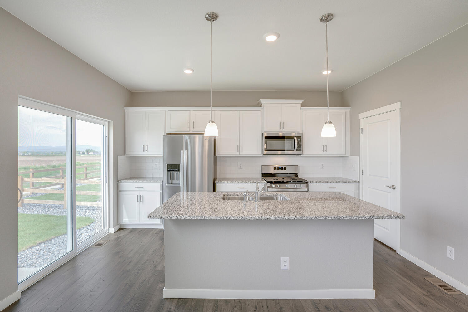 straight view of a white cabinet kitchen with stainless steel appliances, a back door and an island