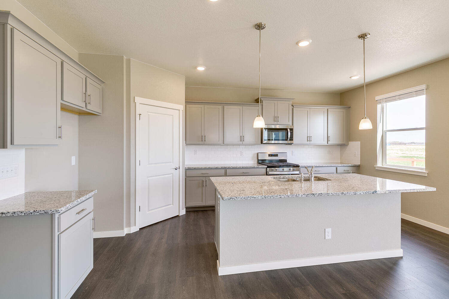 side view of a gray cabinet kitchen with stainless steel appliances, a window, and an island