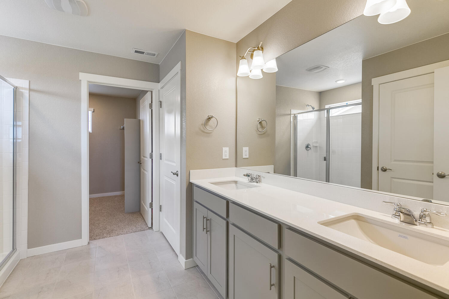 gray cabinet bathroom with dual-basin sink, a shower, tile floor, and white doors
