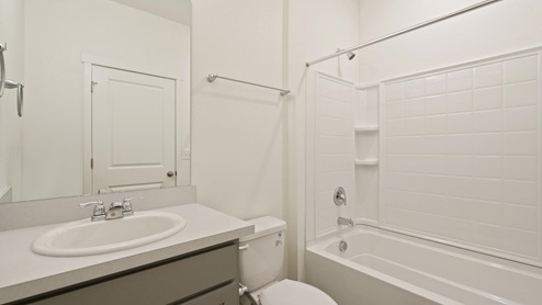 gray cabinet bathroom with a tub, toilet and a sink