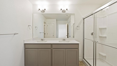 bathroom with gray cabinet, a shower, and dual-basin sinks