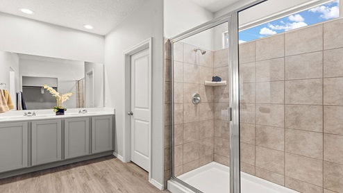 primary bathroom with shower and vanity with gray cabinets and white quartz countertop
