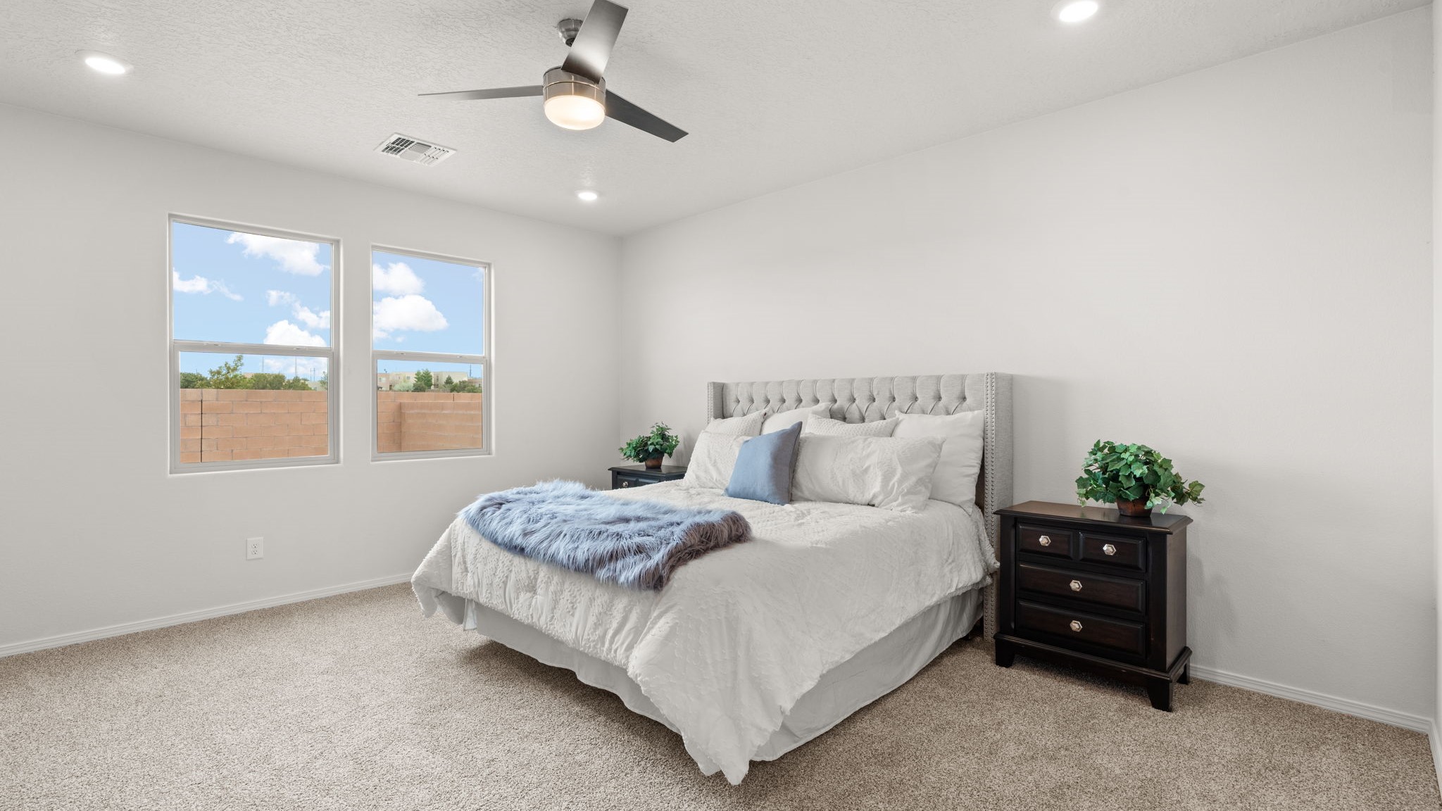 Downstairs primary suite with carpet, ceiling fan, and two winodws overlooking backyard.
