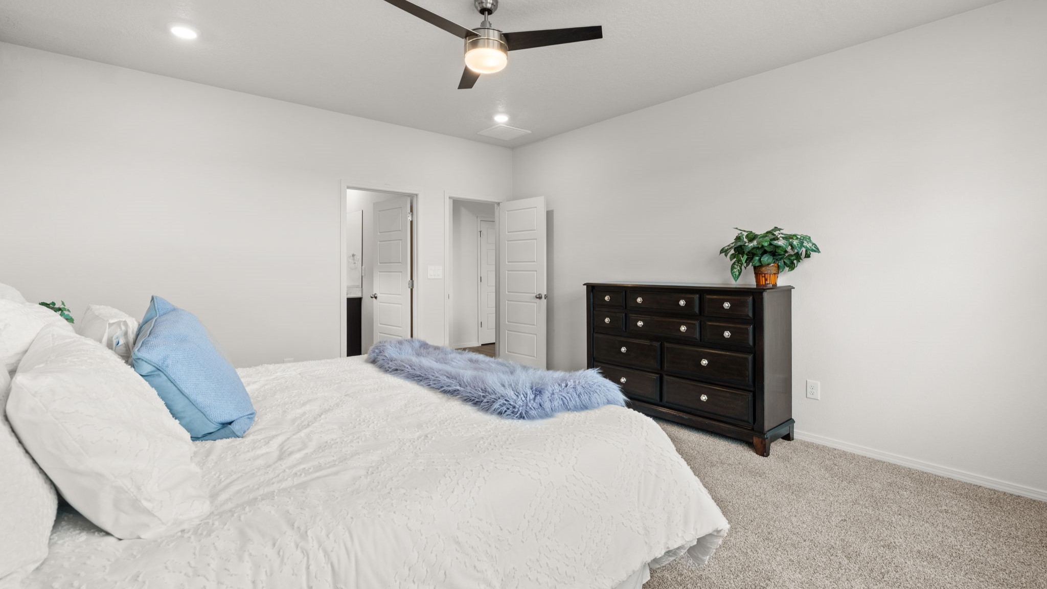 Downstairs primary suite with carpet, ceiling fan, and two winodws overlooking backyard.