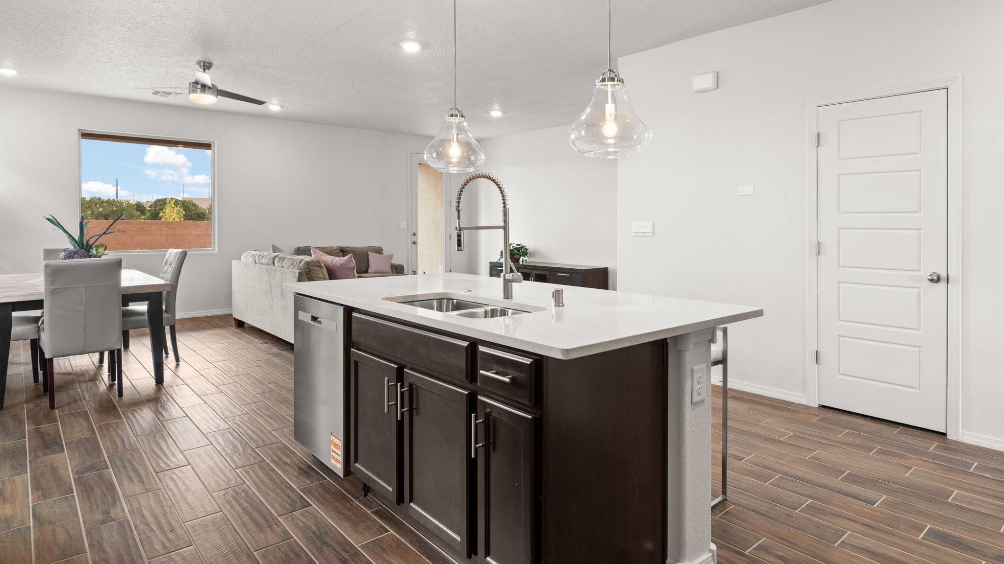 .Bliss kitchen with brown cabinets, tile floors, kitchen island with sink, and granite countertops.