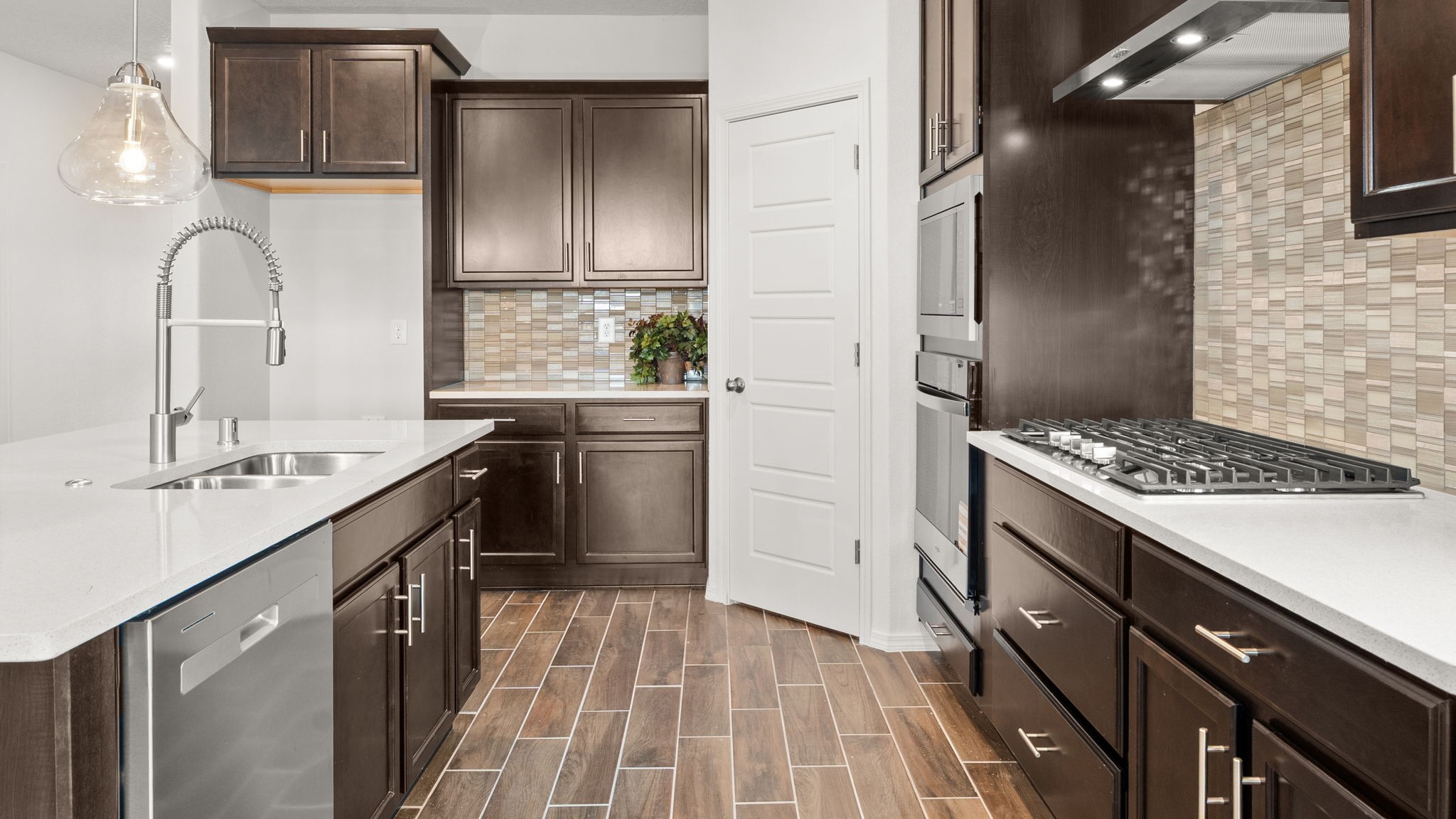 .Bliss kitchen with brown cabinets, tile floors, kitchen island with sink, and granite countertops.