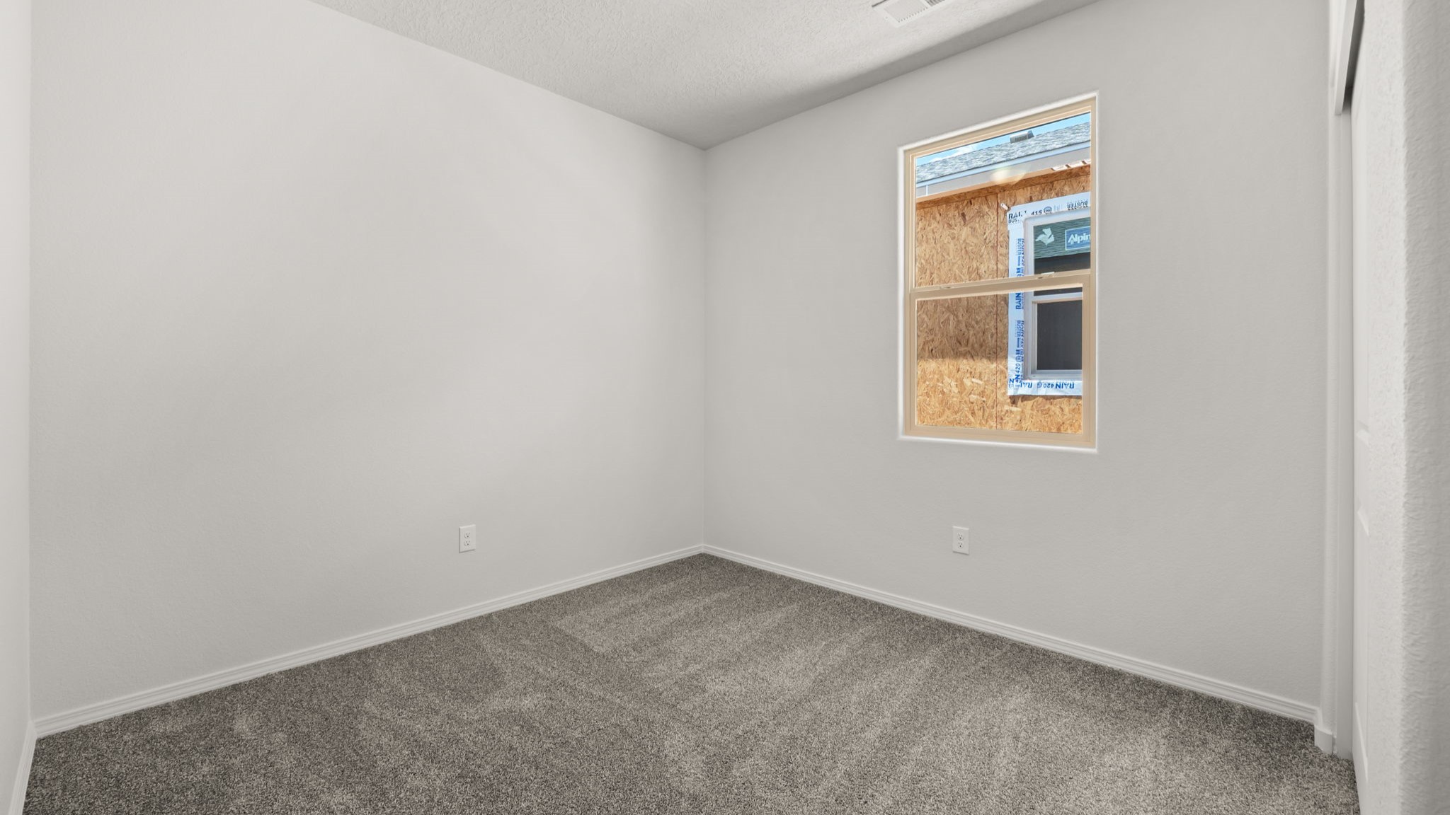 Bedroom with white walls, brown carpet, and windows.