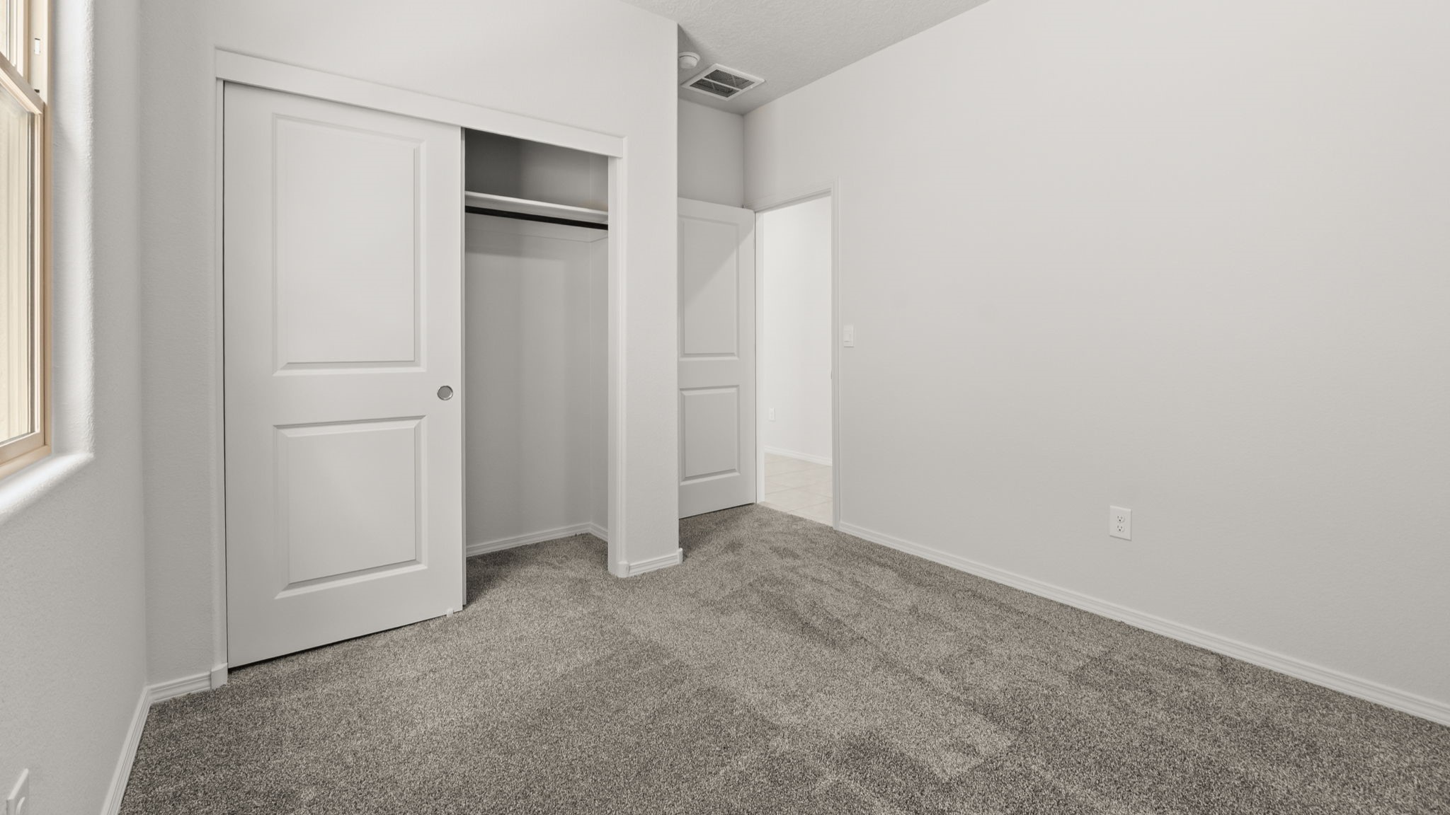 Bedroom with white walls, brown carpet, and a closet.