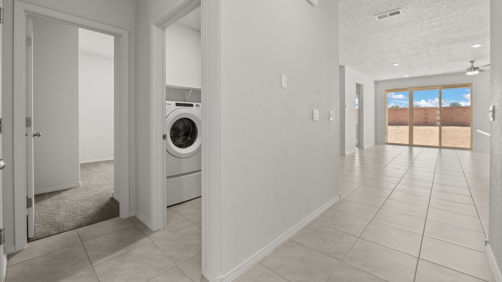 Doorway to laundry room and a bedroom with white walls and light brown tile.
