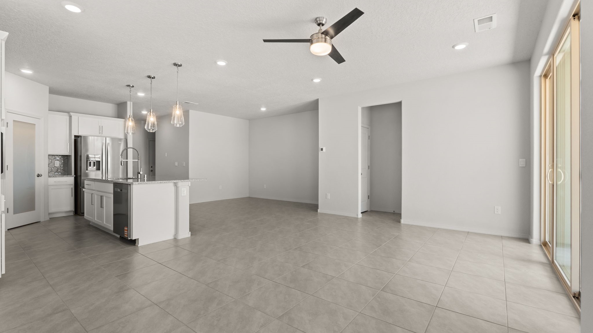 Living area with white walls, brown tile, and a large sliding door,