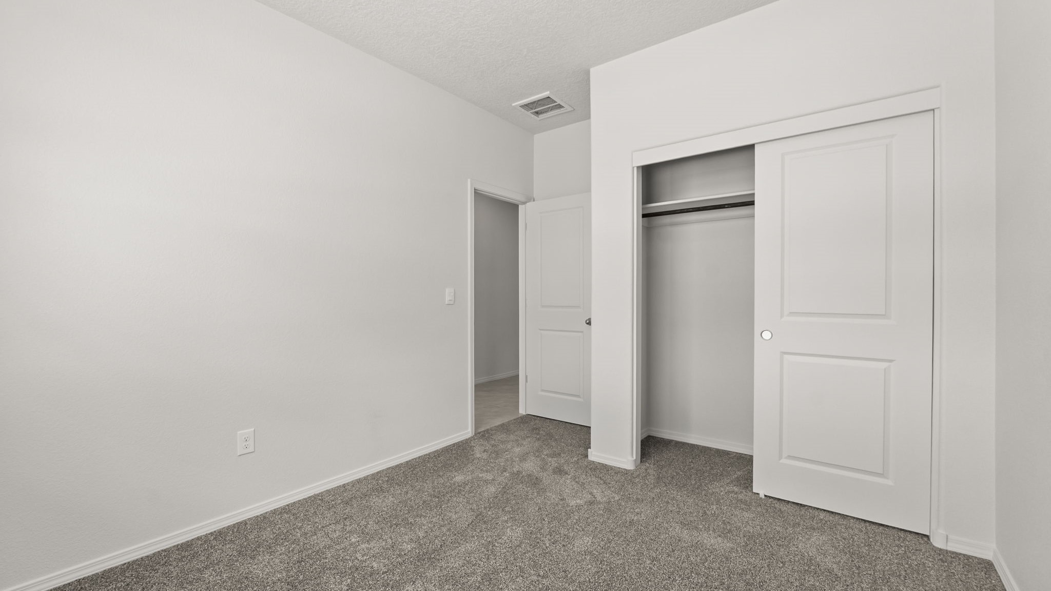 Bedroom with white walls, brown carpet, and a closet.