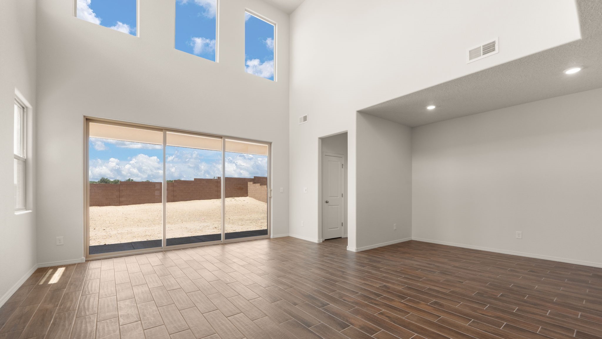 Living room area with brown wood floors, white walls, and a large sliding door..