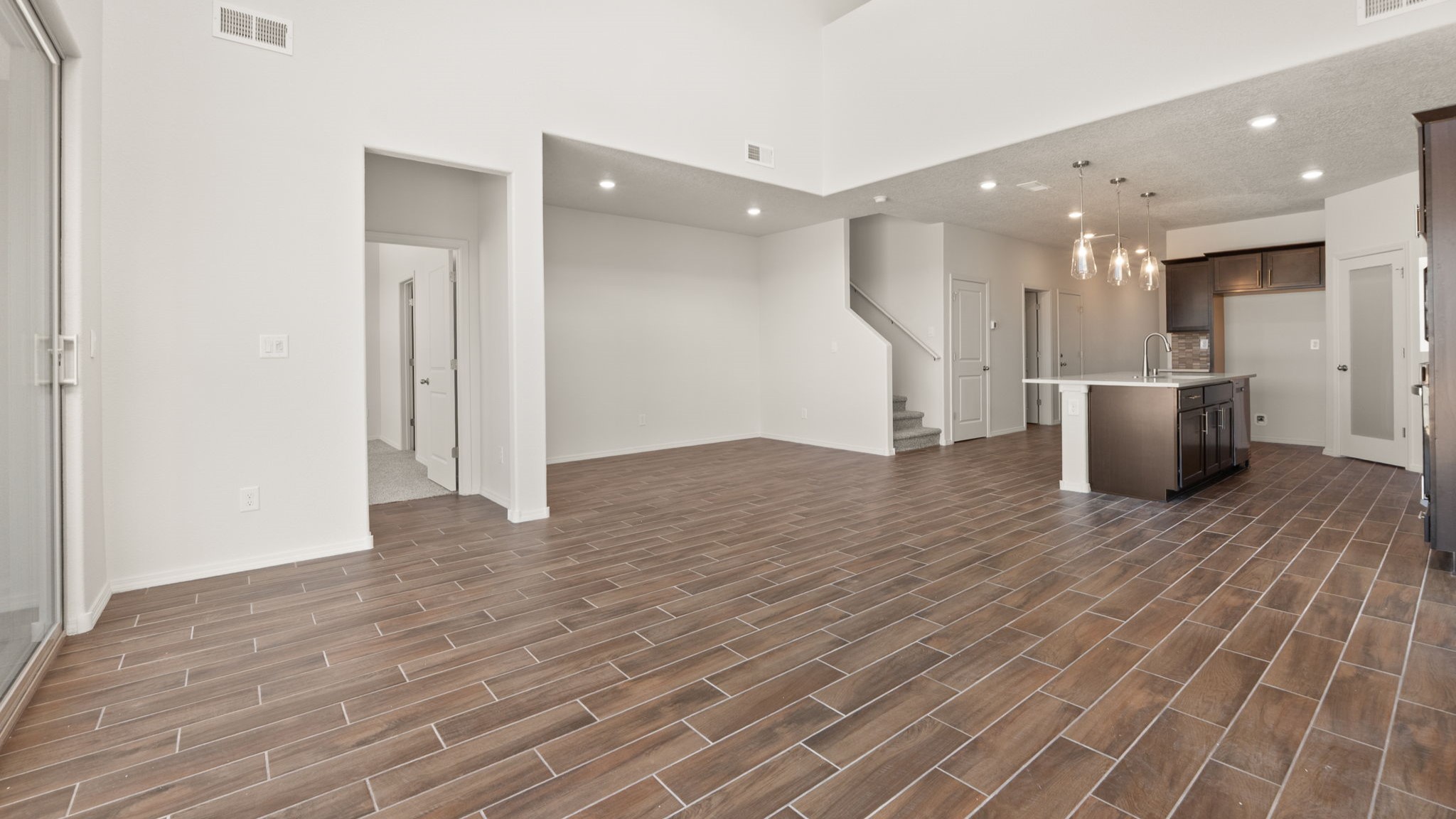 Living room area with brown wood floors, white walls, and a large sliding door..