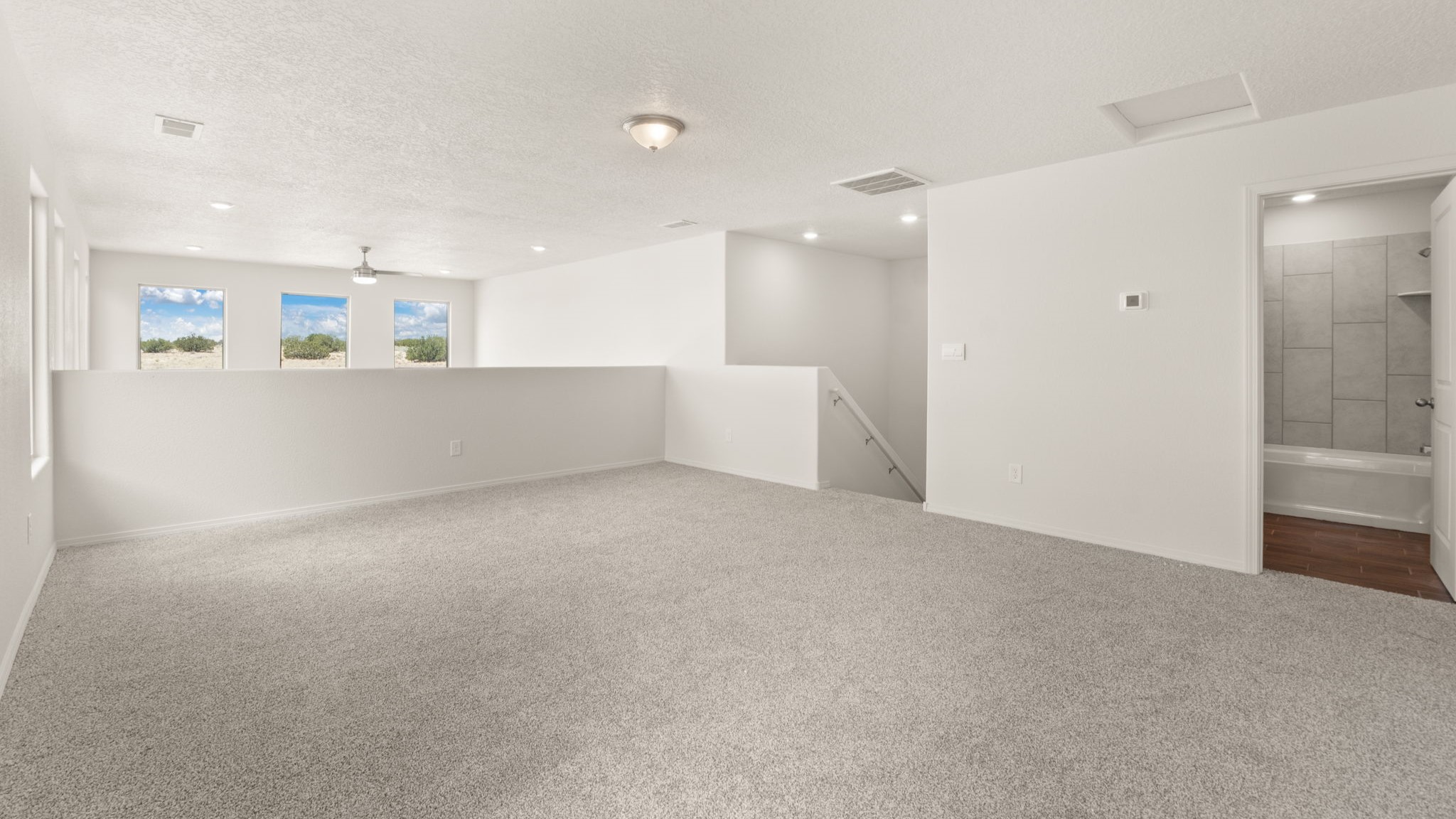 Area at the top of the stairs with brown carpet, white walls, and a bathroom.